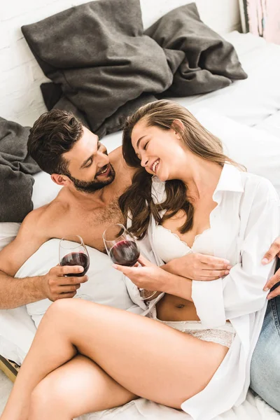 Joven Pareja Sentada Cama Sonriendo Mientras Bebe Vino —  Fotos de Stock