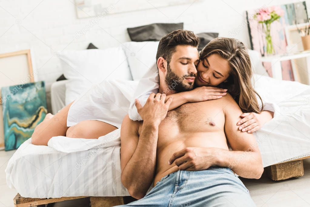young girl lying in bed and hugging man while guy sitting on floor near bed