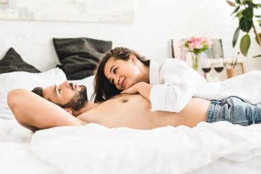 Genç çift yatakta yatarken kız gülümseyen ve adam bakıyor