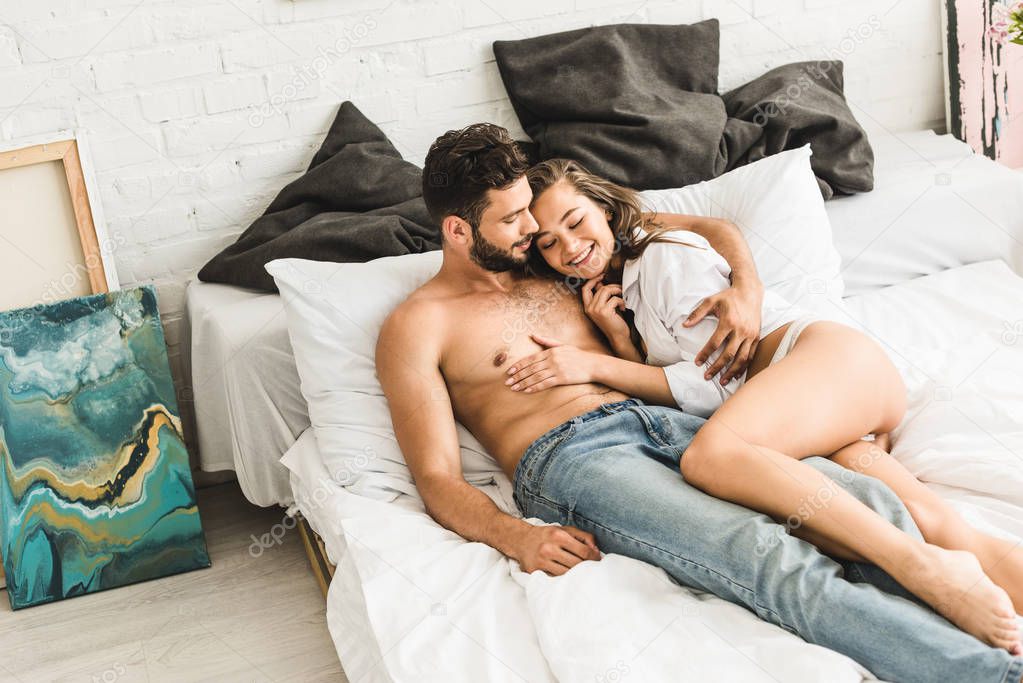 sexy couple lying in bed and smiling while girl touching shirtless man