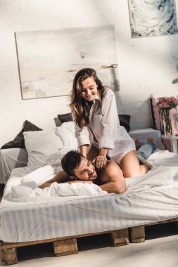 seksi mutlu çift yatakta yatıyor iken kız arka üzerinde oturuyor gömleksiz adam 