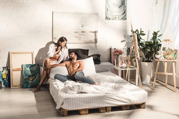 性感的夫妇坐在床上 看着对方 而男人躺在床上 — 图库照片