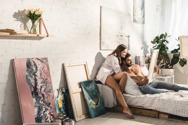 幸福的年轻夫妇坐在床上 看着绘画 — 图库照片
