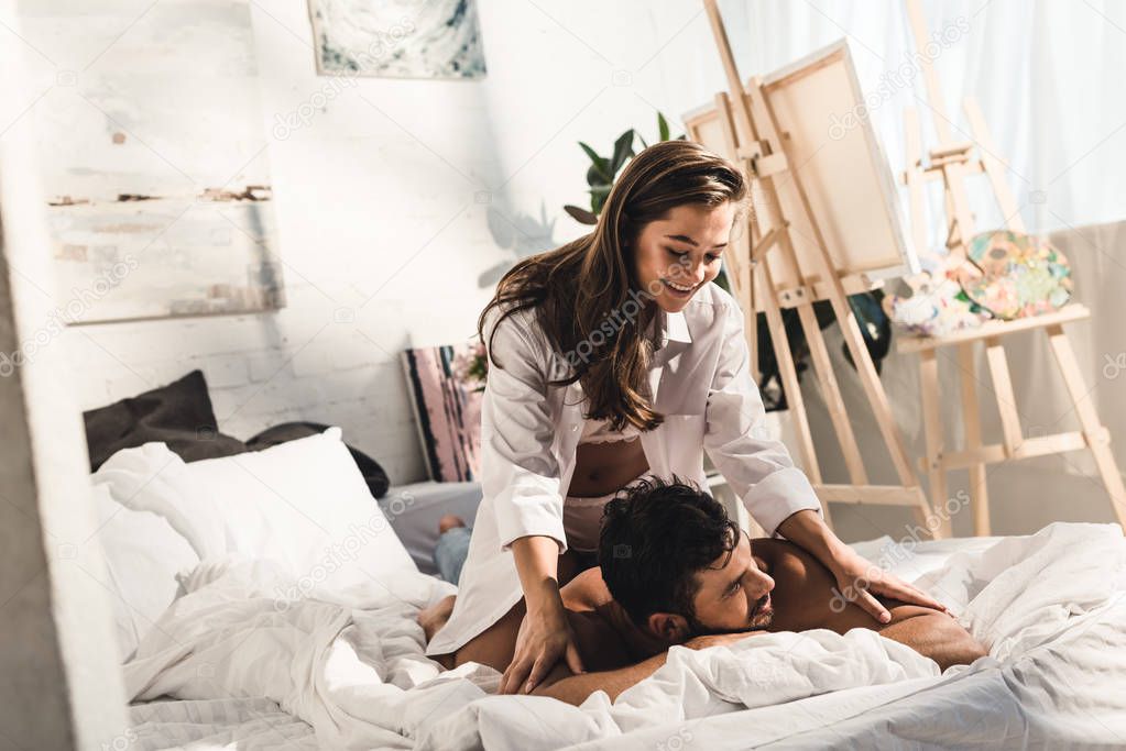 happy young couple laughing while girl in white underwear sitting on back of shirtless man