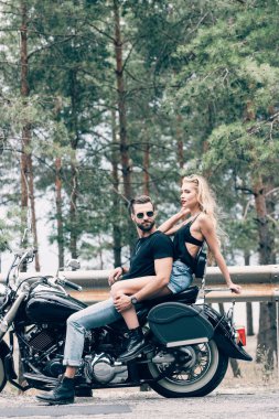yeşil orman yakınındaki yolda siyah motosiklet üzerinde bisikletçilerin seksi çift yan görünümü