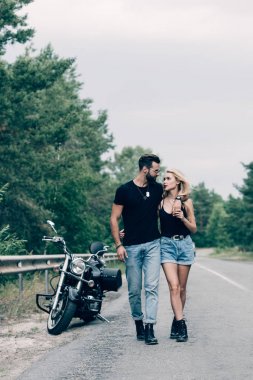 bisikletçileri genç çift yol boyunca yürüyüş ve siyah motosiklet yakınında kucaklayan