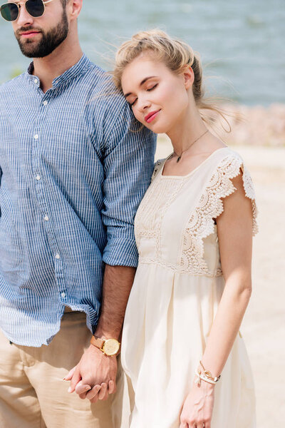 blonde girl with closed eyes leaning on boyfriend shoulder at beach