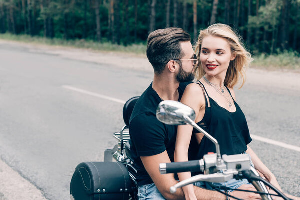 счастливая молодая пара байкеров глядя друг на друга на черном мотоцикле на дороге
