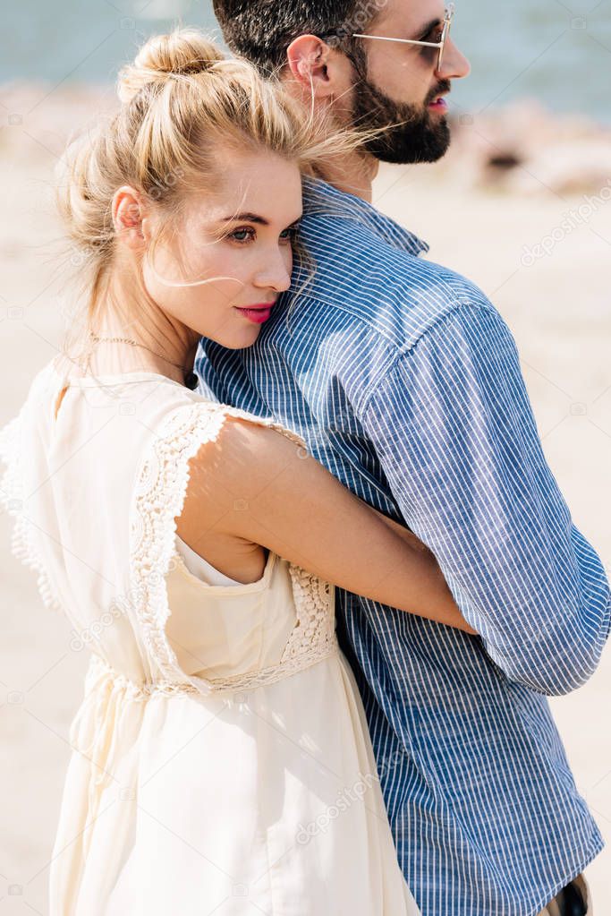 young blonde woman hugging bearded boyfriend at beach