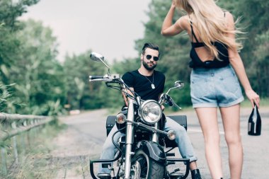 siyah motosiklet üzerinde güneş gözlüğü yakışıklı erkek arkadaşı yakın alkol şişesi ile yolda yürüyen genç kadının arka görünümü