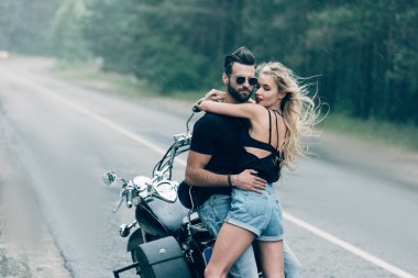 yeşil orman yakınındaki yolda siyah motosiklet yakın kucaklayan motosiklet genç seksi çift