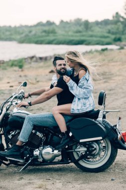 kumlu plajda siyah motosiklet üzerinde sarılma bisikletçileri gülümseyen genç çift