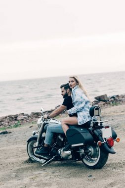 nehir yakınındaki plajda siyah motosiklet üzerinde oturan bisikletçilerin genç sevgi dolu çift