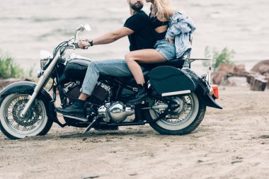 kumlu plajda siyah motosiklet üzerinde bisikletçilerin seksi genç çift kırpılmış görünümü