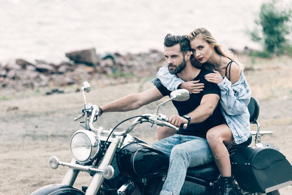 young couple of bikers embracing on black motorcycle at sandy beach