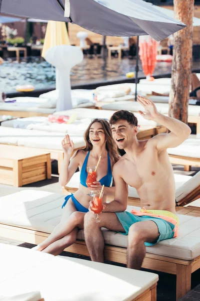 Cheerful Young Couple Waving Hands While Sitting Deck Chair Glasses — Stock Photo, Image