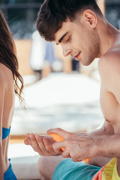 Bonito Jovem Aplicando Protetor Solar Loção Mão Perto Sentado Namorada — Fotografia de Stock