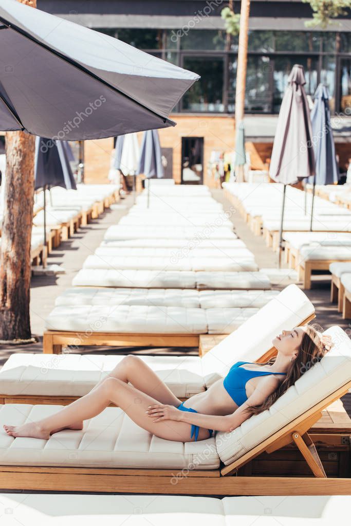 beautiful young woman sunbathing on chaise lounge with closed eyes