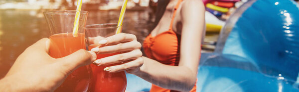 cropped view of young couple clinking glasses with refreshing drink, panoramic shot 
