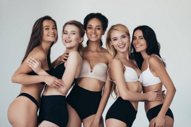 five sexy multiethnic girls in lingerie embracing and smiling isolated on grey clipart
