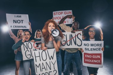 redhead girl holding placard with how many more lettering and screaming in megaphone near multicultural people on black  clipart