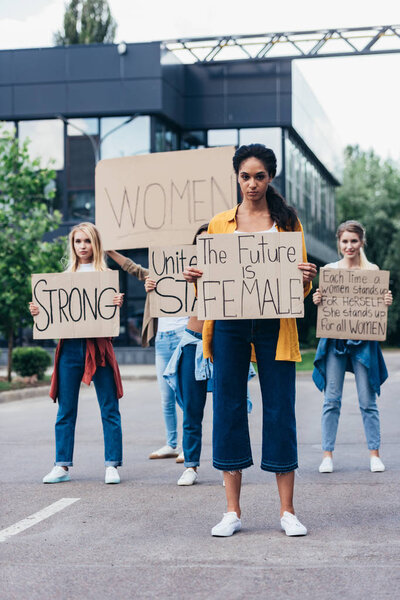 full length view of african american feminist holding placard with inscription the future is female near women on street