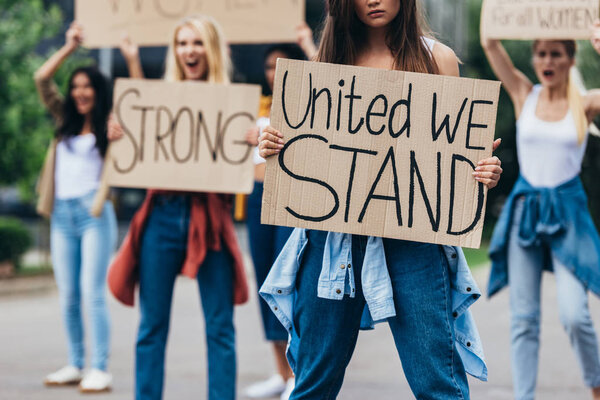 cropped view of girl holding placard with inscription united we stand near feminists on street