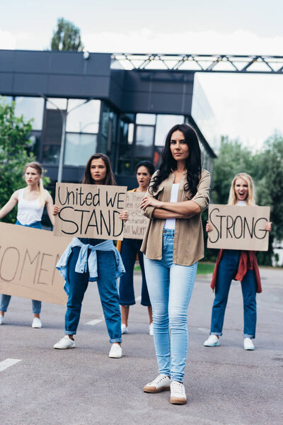 full length view of woman standing near feminists holding placards with slogans on street