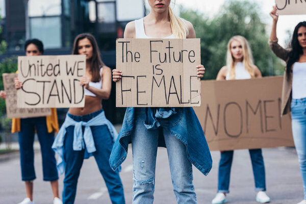 cropped view of woman holding placard with inscription the future is female near feminists on street