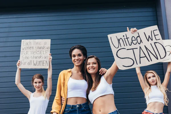 Four Smiling Multiethnic Feminists Embracing Holding Placards Slogans Street — Stock Photo, Image