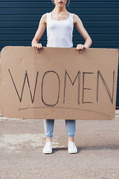 cropped view of feminist with word brave on body holding placard with inscription women on street