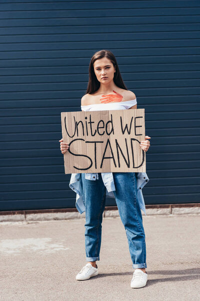 full length view of feminist holding placard with inscription united we stand on street