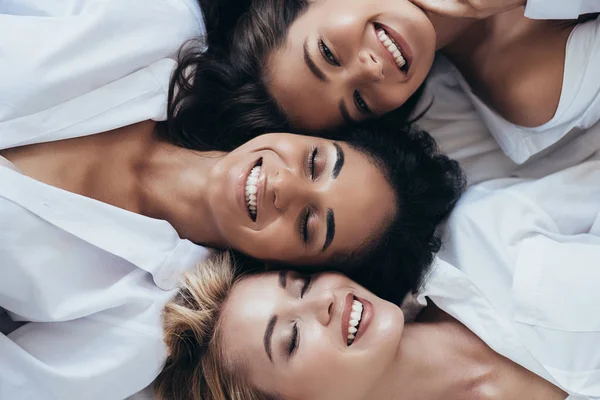 Widok Góry Trzy Uśmiechnięte Wieloetniczne Kobiety Białych Koszulkach Leżących Zamkniętymi — Zdjęcie stockowe