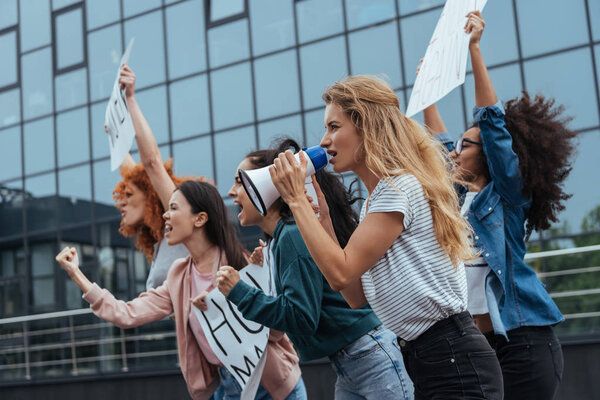 selective focus of girl with megaphone near multicultural women holding placards on meeting 