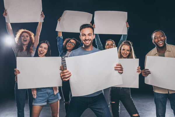 positive multicultural people screaming while holding blank placards on black 