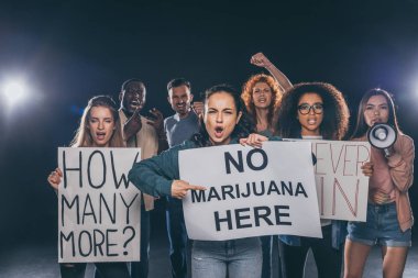 emotional girl pointing with finger at placard with no marijuana here lettering near multicultural people on black  clipart