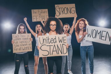 beautiful multicultural women standing and holding placards on black   clipart