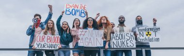 panoramic shot of men with scarfs on faces gesturing near multicultural people with placards  clipart