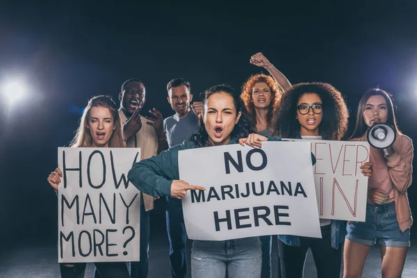 emotional girl pointing with finger at placard with no marijuana here lettering near multicultural people on black