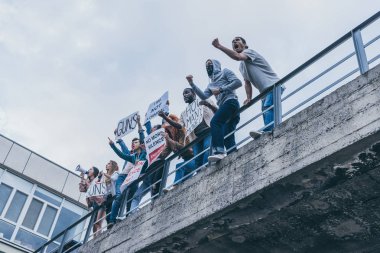 low angle view of multicultural people screaming and gesturing while holding placards  clipart