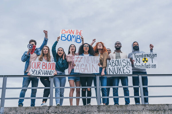 низкий угол обзора мужчин с шарфами на лицах, жестикулирующих рядом с мультикультурными людьми с надписью на плакатах
 