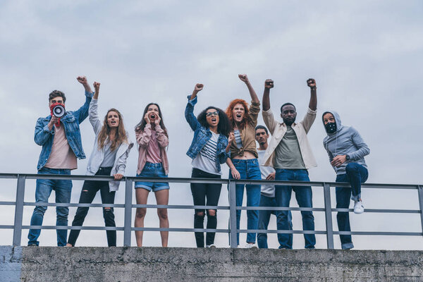 men with scarfs on faces gesturing near multicultural people screaming outside 
