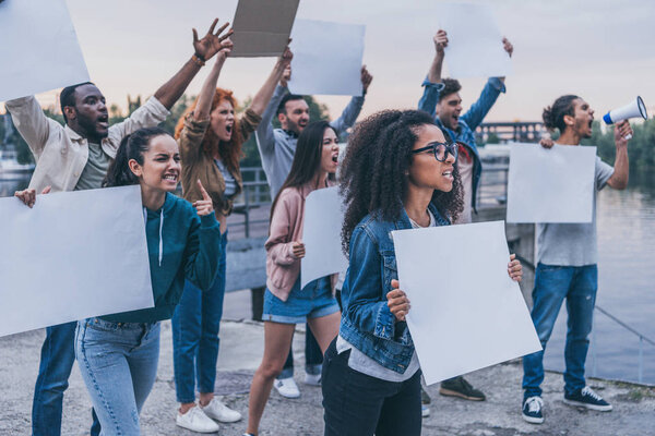 selective focus of emotional multicultural people holding blank placards 