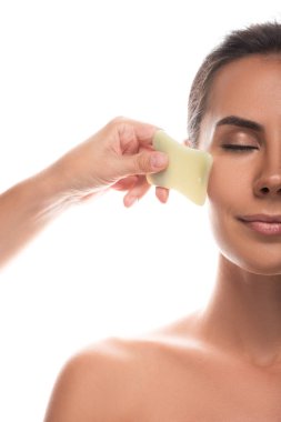 cropped view of nude young woman using gua sha scraper with closed eyes isolated on white clipart