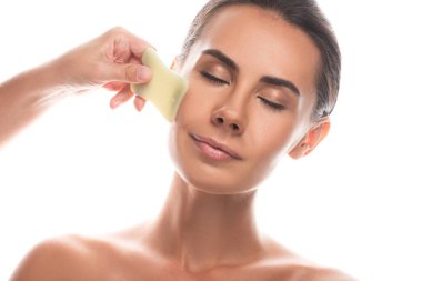 nude young woman using gua sha scraper with closed eyes isolated on white clipart