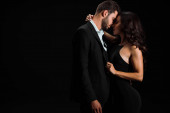 attraktive Frau berührt Anzug des Mannes, während sie isoliert auf schwarz steht 