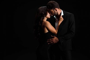 attractive girl touching suit of passionate bearded man isolated on black  clipart