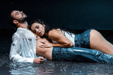 sexy and wet woman lying with handsome boyfriend under raindrops on black  clipart