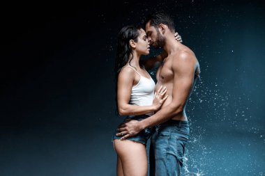 sexy shirtless man hugging attractive woman near splash of water on black  clipart