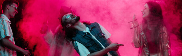 панорамный снимок танцующих в ночном клубе мужчин и девочек с розовым дымом
